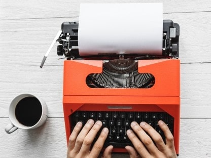 Photo of an orange typewriter on a desk, with a nice cup of tea