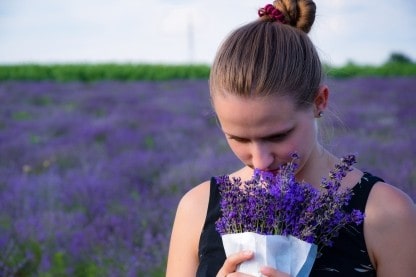 A woman smelling flowers beside a field of purple flowers