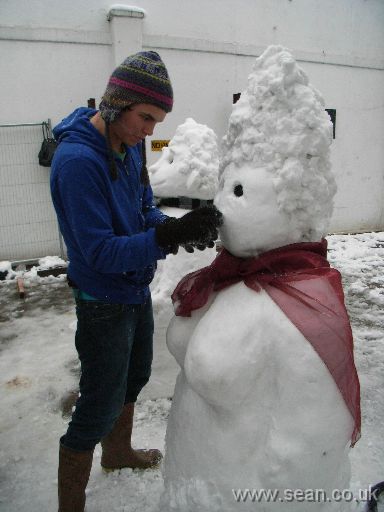 Man carving nose of snow-woman with knife