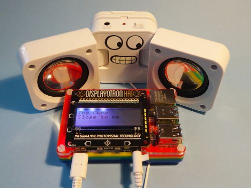 A photo of my Raspberry Radio setup, with white ipod speakers connected to the Raspberry Pi, and a Display-O-Tron HAT showing the artist and song title.