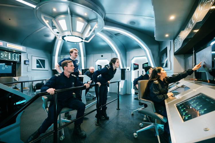 A view from the corner of the spaceship bridge. The crew monitor a screen with concern.